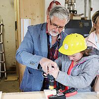 Foto zeigt Impression aus dem Projekttag "Kleine Baumeister" mit Architekt Dittrich, Kind mit gelbem Bauhelm