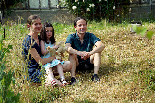 Die Eltern sitzen mit der kleinen Esther im Gras vor ihrem Haus.