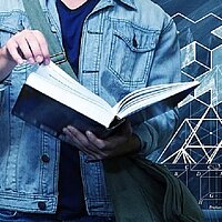 Foto zeigt Student mit einem aufgeschlagenen Buch vor einer Schultafel mit Formeln und Zeichnungen.