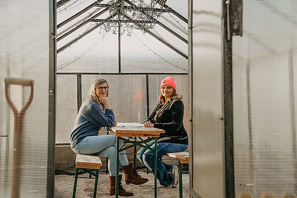 Becky Taylor-Hellwig und Nestbau-Koordinatorin Helen Bauer sitzen im Gewächshaus im Garten