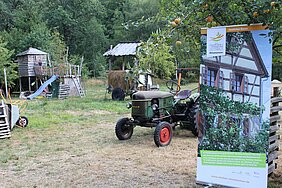 Foto zeigt Wiese mit grünem Traktor und einem Plakat von der Nestbau-Zentrale.