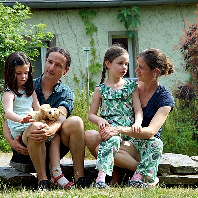 Andreas und Gerlinde Feller mit ihren Töchtern Esther und Leonore auf einer Steinmauer sitzend.