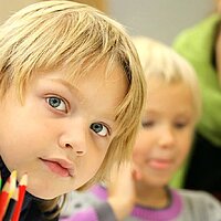 Kinder in der Schule: Foto zeigt das Portrait eines Kindes mit farbigen Buntstiften im Vordergrund.