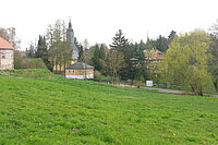 Foto zeigt eine grüne Wiese im Hintergrund eine Kirche, Wald und Häuser