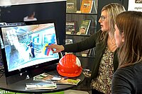 Helen Bauer zeigt auf einen Bildschirm, auf dem das virtuelle Mittelsächsische Haus zu sehen ist.