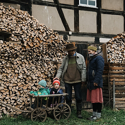 Familie Häuser Freymann mit ihren zwei Kindern im Fachwerkhof. Die Kinder sitzen in einem Holzwagen