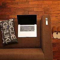 Arbeiten zu Hause: Fotom zeigt Featurebild mit Sofa, Laptop, Hausschuhen und Kuschelkissen.