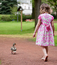 Landidylle: Foto zeigt ein kleines Mädchen in einem geblümten Kleid. das Kind läuft barfuss einen Weg entlang. Vorneweg läuft eine Ente.