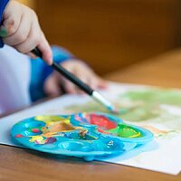 Fotom zeigt Kleinkind bei der Freizeitbeschäftigung. Kinderhände mit Mischpalette und verschiedenen Farben beim Malen.
