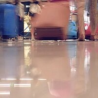 Foto zeigt ein symbolisches Bild für den Begriff Ankommen: Füße und Rollkoffer in Bahnhofs- oder Flughafenatmosphäre. Spiegelung auf blank-glänzendem Fußboden.