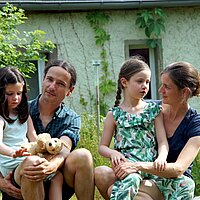 Familie Feller gemeinsam mit den Töchtern auf einer Steinmauer sitzend im Garten